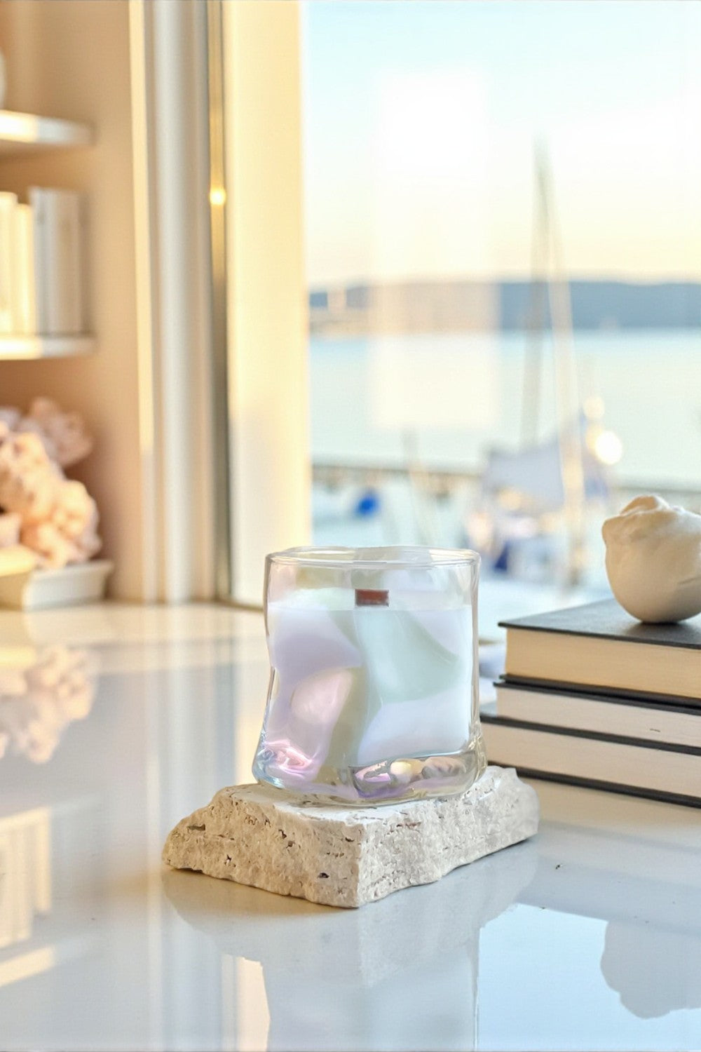 Glass candle holder with a pink candle on a stone base in a bright room with books and decor.