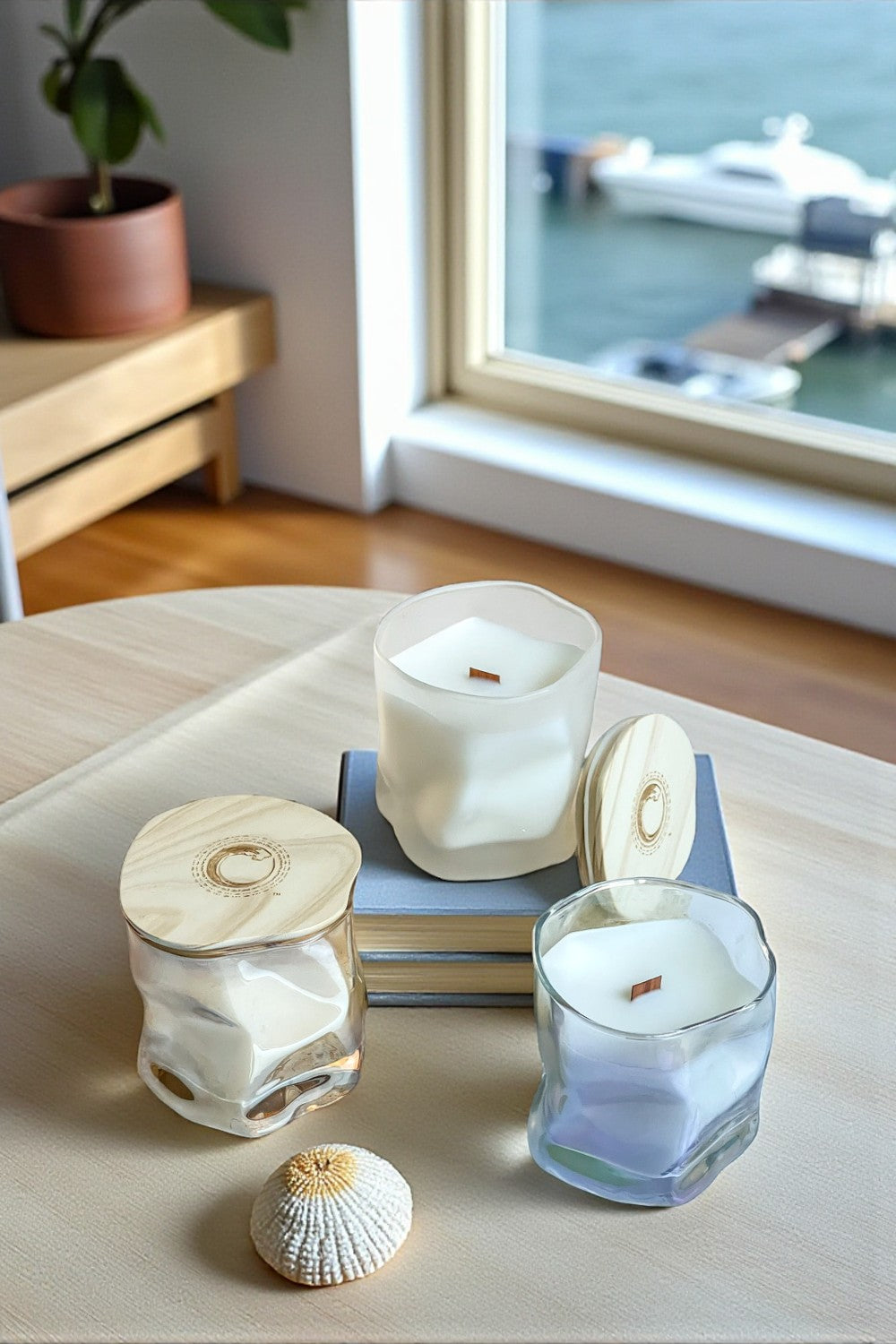 Candle holders with seashell designs on a table by a window with a view of water.