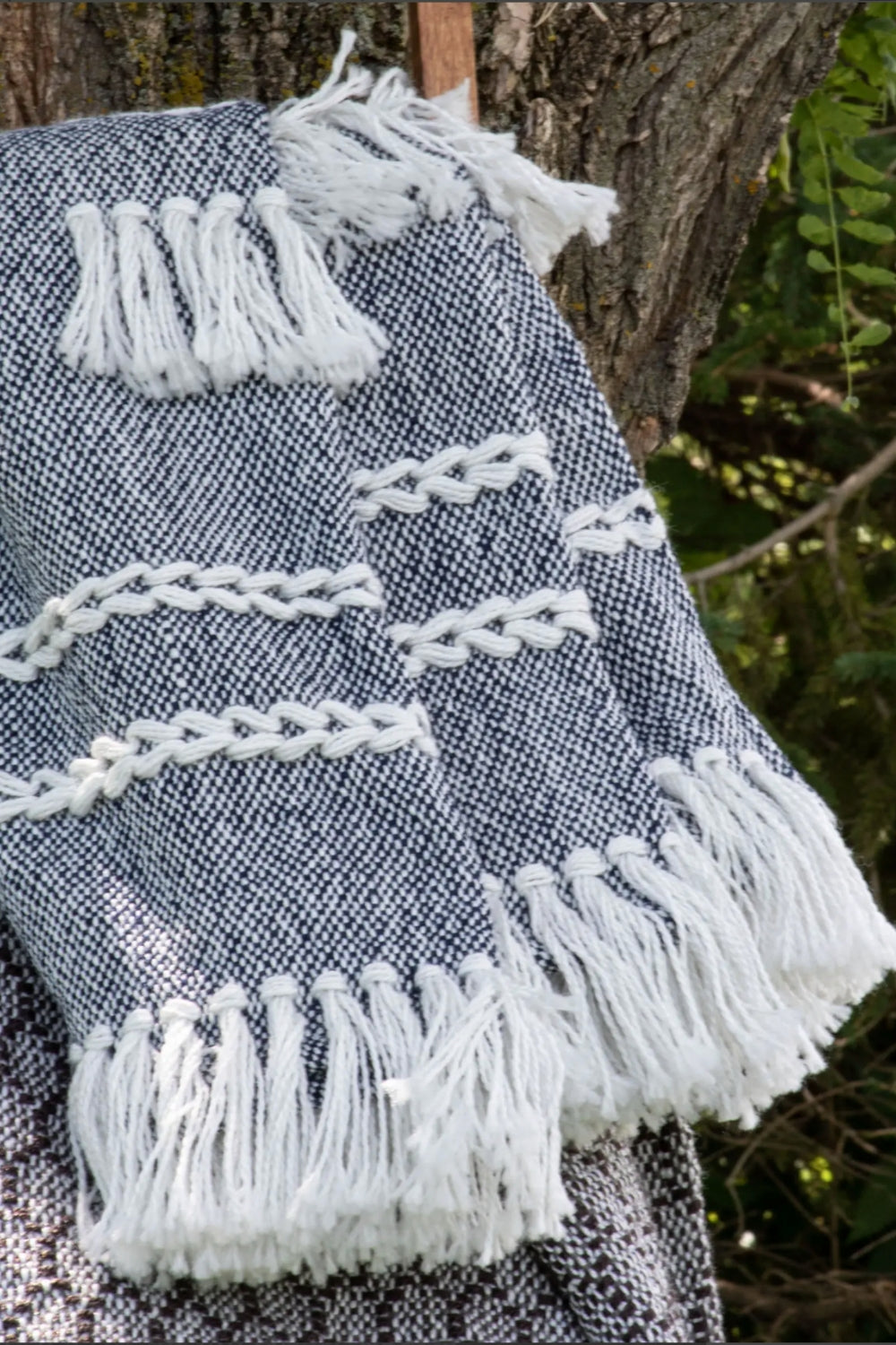 Textured fabric with white fringe details draped over a tree branch.