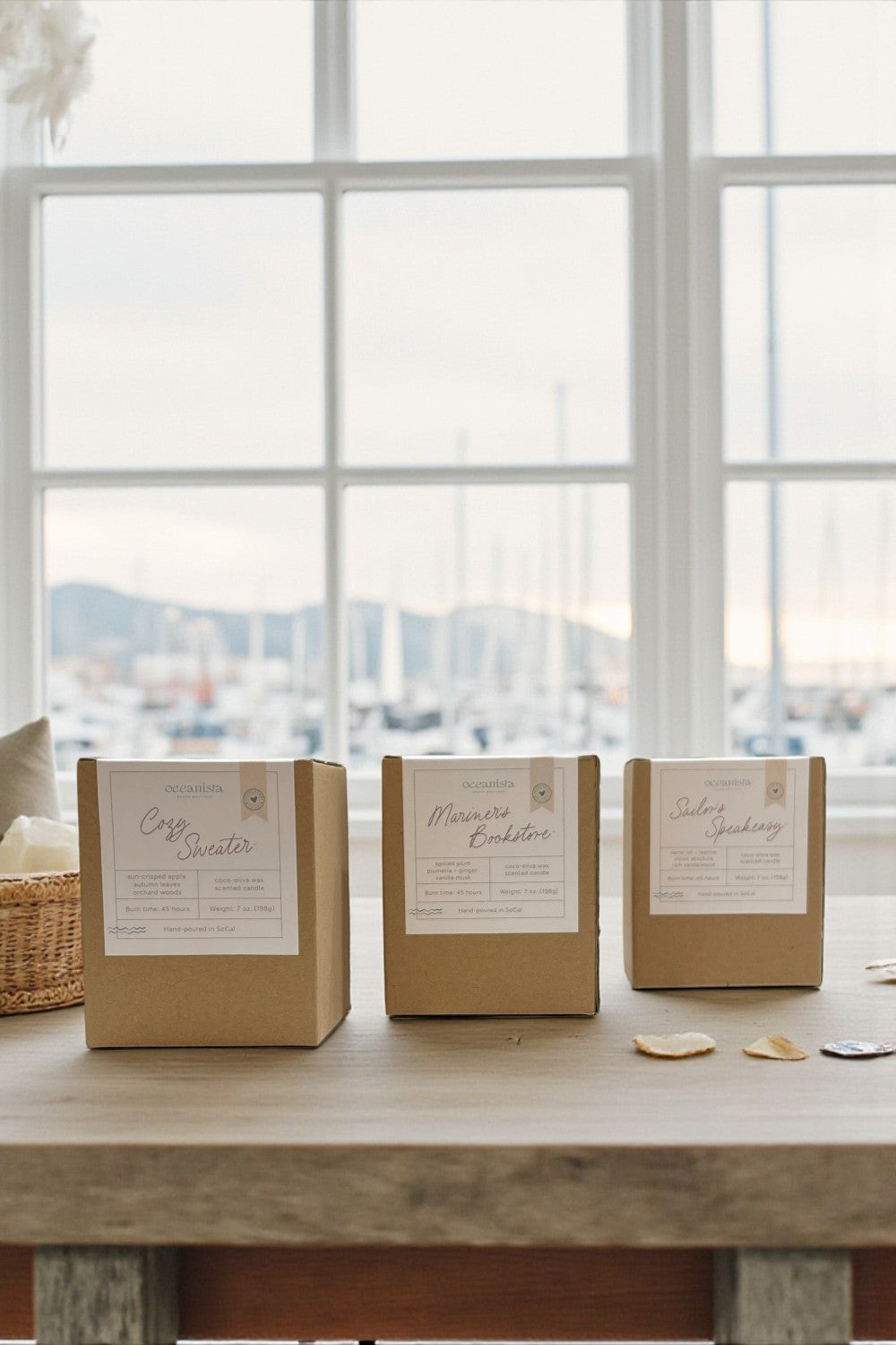 Three brown boxes with labels on a wooden table by a window with a view of water.